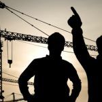 workers in hard hats at construction site pointing to crane