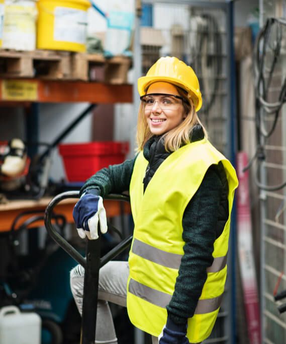 A worker wearing protective equipment smiles next to a pallet jack