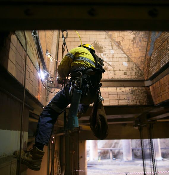 A worker lowered into a confined space with a safety harness