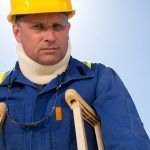 worker in hard hat and safety glasses wearing neck brace on crutches