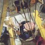 worker in hard hat on harness being lowered into well