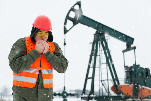 man warms hands beside oil rig