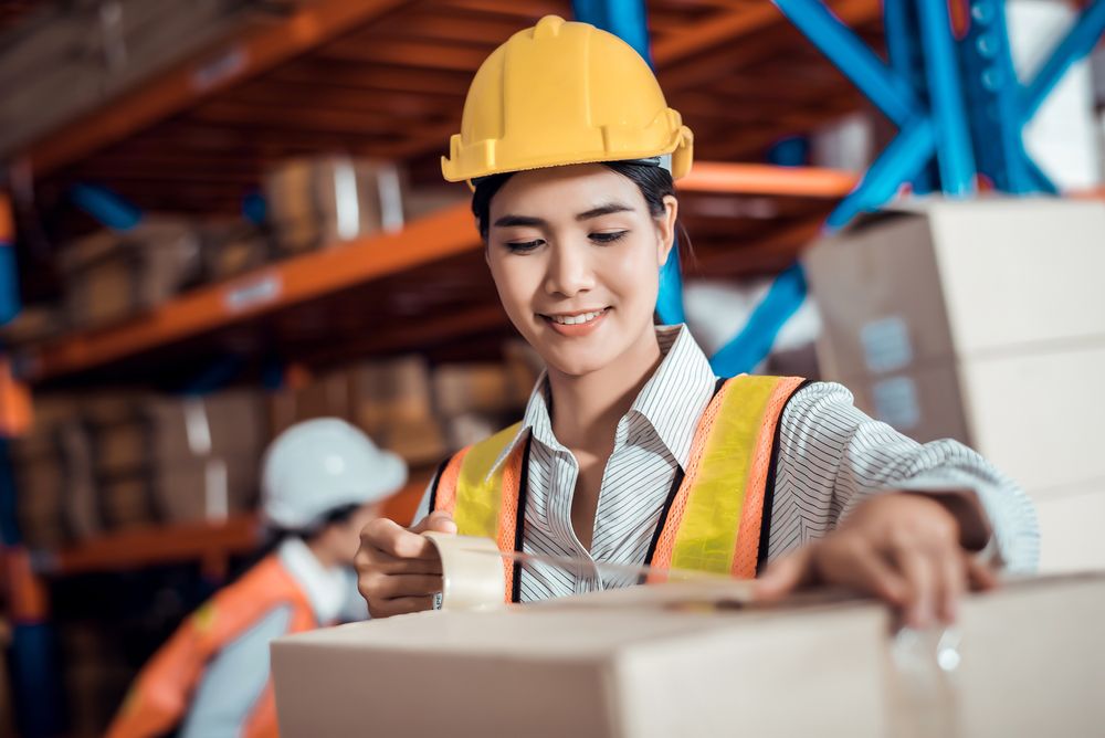 a female warehouse worker taping up a box while smiling