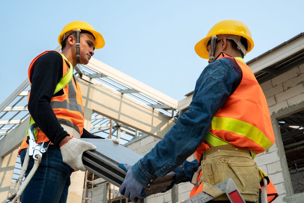 two construction workers lifting a piece of heavy material together to avoid injury