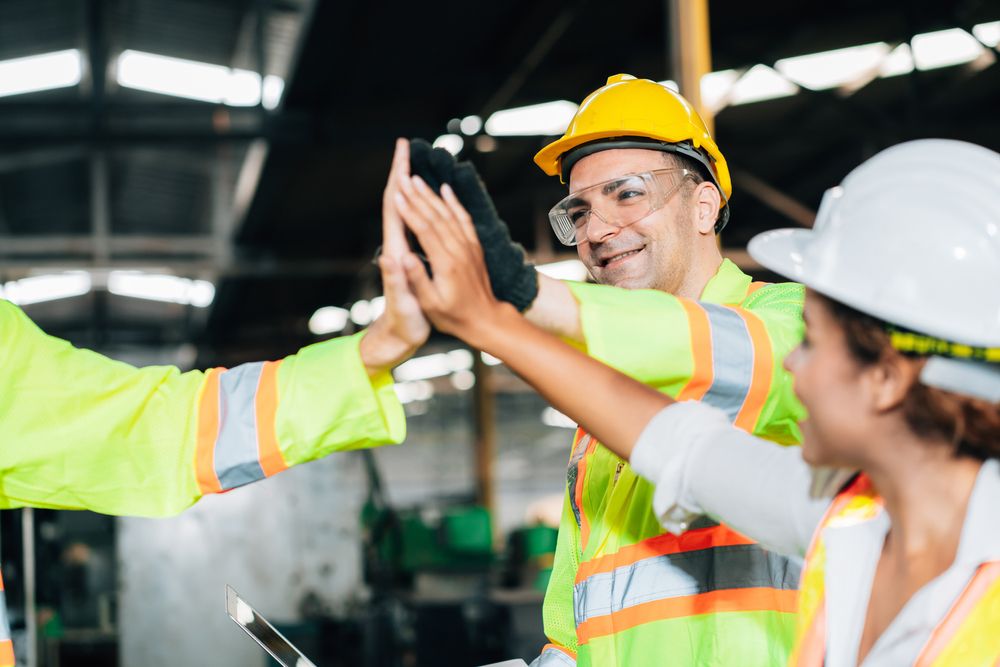 three warehouse employees on the safety committee giving each other a high-five.
