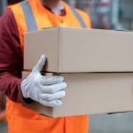 warehouse worker carrying cardboard boxes wearing white gloves to avoid injury