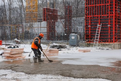 A Worker In Overalls Leveling Concrete At A Construction- Winter Safety