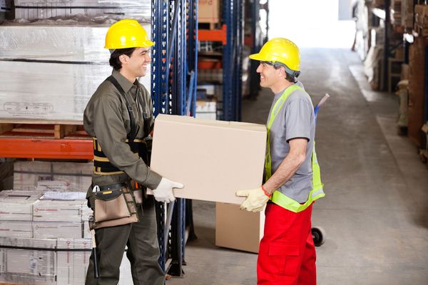 men in hard hats carry box in warehouse with safety in mind