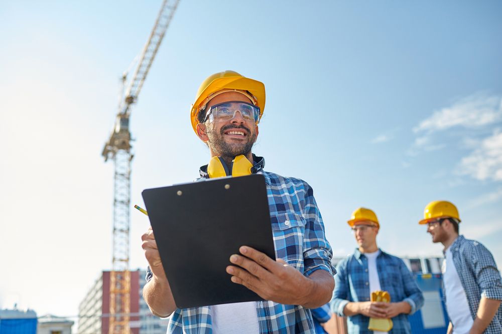 a construction site manager smiling while holding a clipboard - showing a positive workplace culture