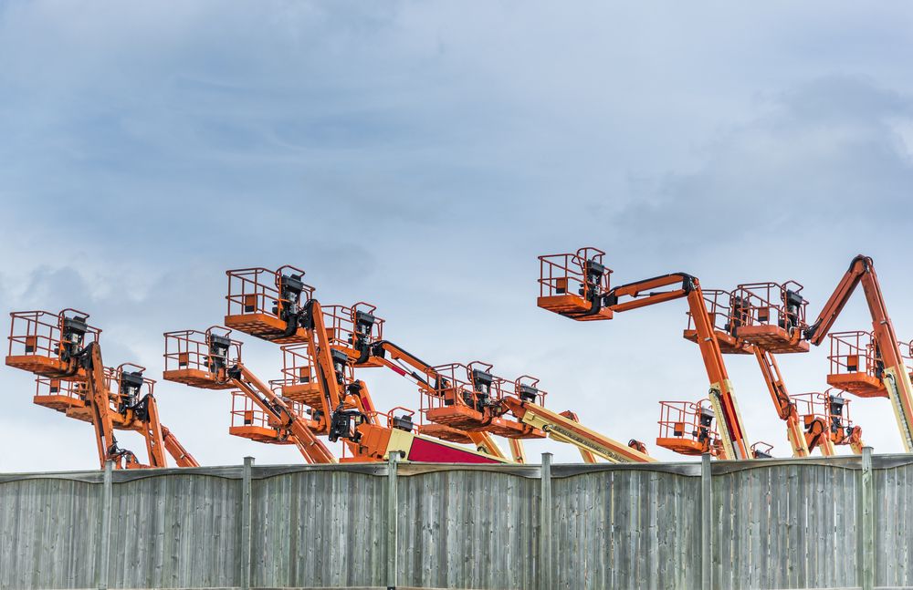 several orange aerial lifts parked at a construction site