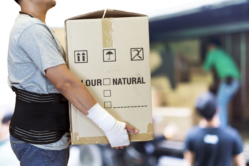 a warehouse worker practicing good workplace ergonomics by using a back brace and gloves to lift boxes