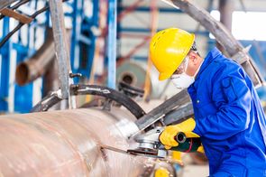 an industrial worker cuts through a large metal pipe