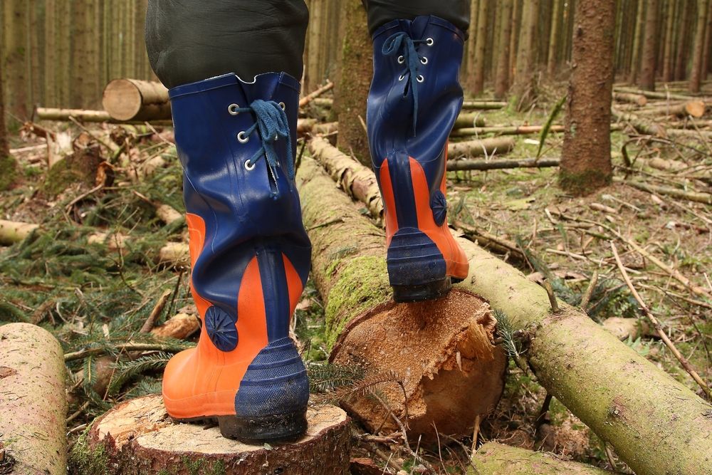 an arborist wearing the proper safety shoes to protect them while standing on a pile of chopped wood.