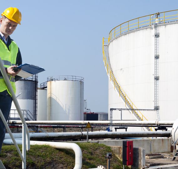 a worker takes notes on a clipboard with large oil terminals in the background