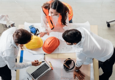 Three construction workers in office clothing going over documents on a table