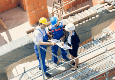 Workers and a manager go over plans while standing on scaffolding